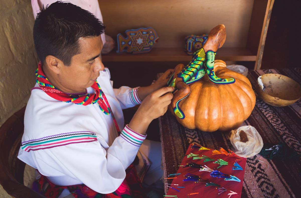 Un indígena mexicano agregando chaquiras a una iguana de madera