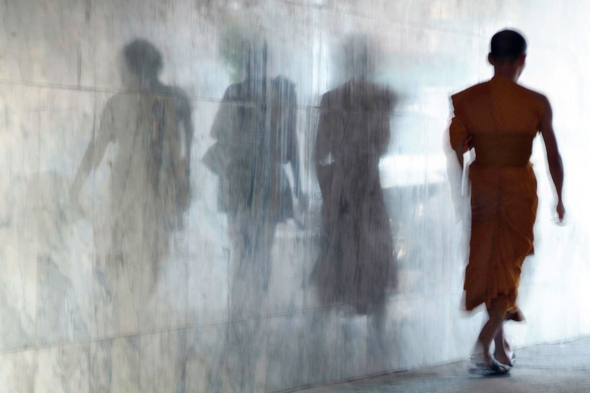 Fotografía de un monje budista caminando, atrás se ven sombras en la pared