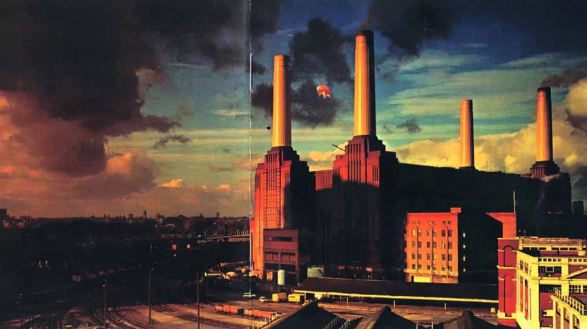 Fotografía de una fábrica en una ciudad con mucho humo en el cielo, la imagen es de tonos naraja.