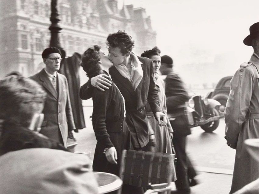En la fotografía dos jóvenes besandose en medio de personas transitando en París.