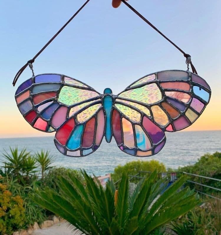 Vitral de colores con forma de mariposa, detrás está el mar abierto.