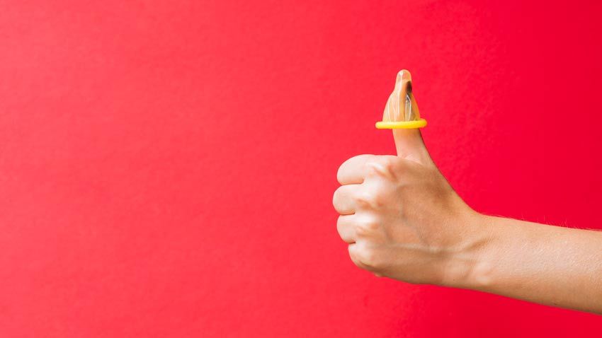 En la imagen, una mano sosteniendo la punta de un condón en el dedo pulgar.