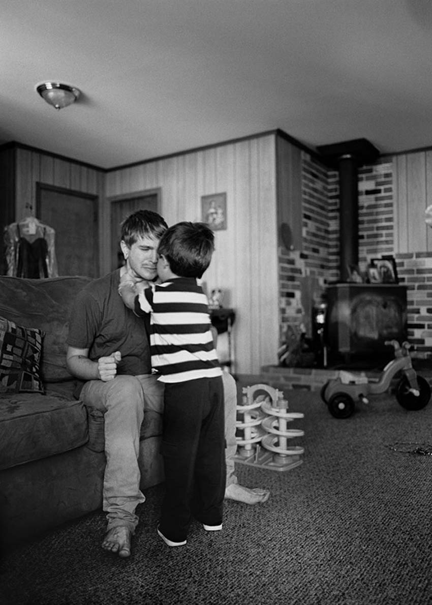 Fotografía en blanco y negro de un niño abrazando a un hombre que está sentado en un sofá de su sala. 