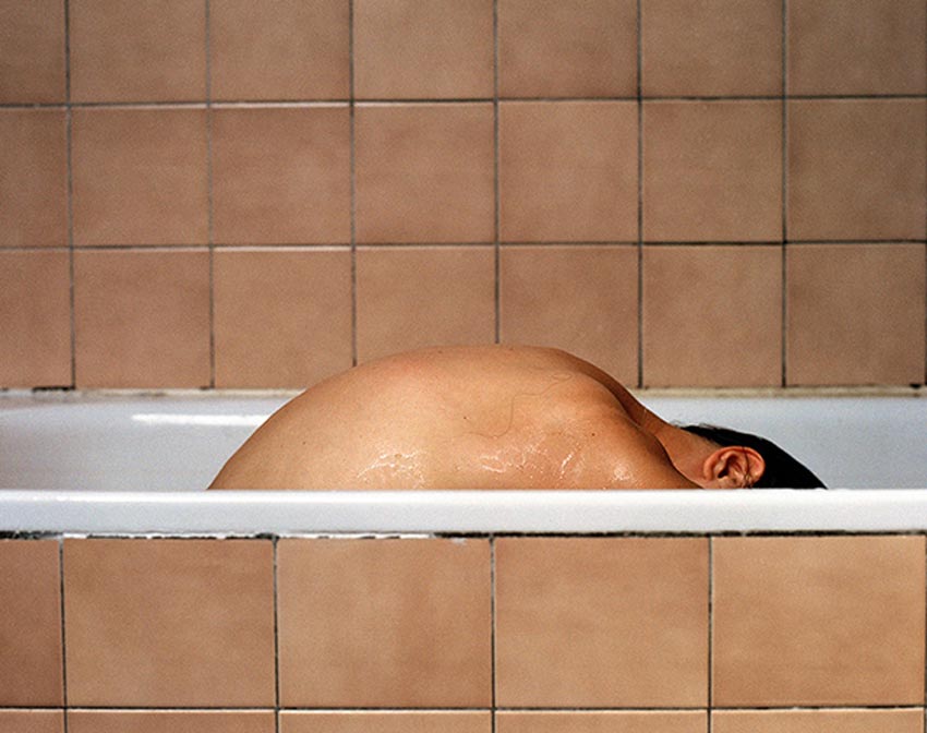 Una persona, aparentemente mujer, dentro de una bañera. Solo se ve su espalda.