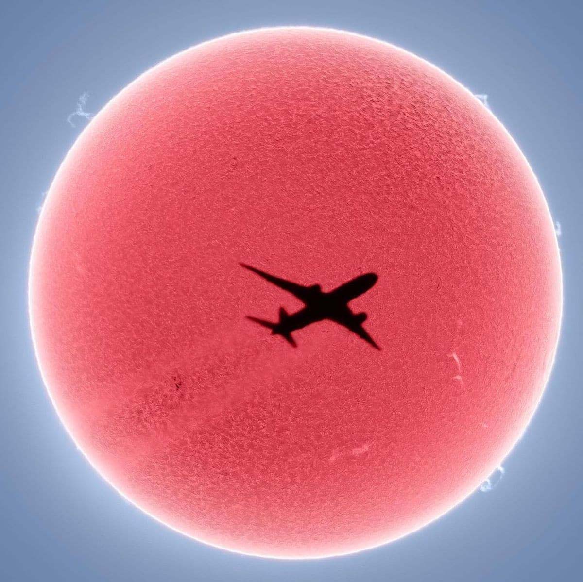 Esfera roja "El Sol" con un avión como sombra en la mitad. Un avión “cruzando” el sol