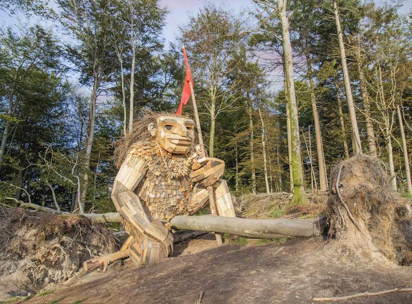 Esculturas de Thomas Dambo gigantes. Troll de rodillas sosteniendo una bandera