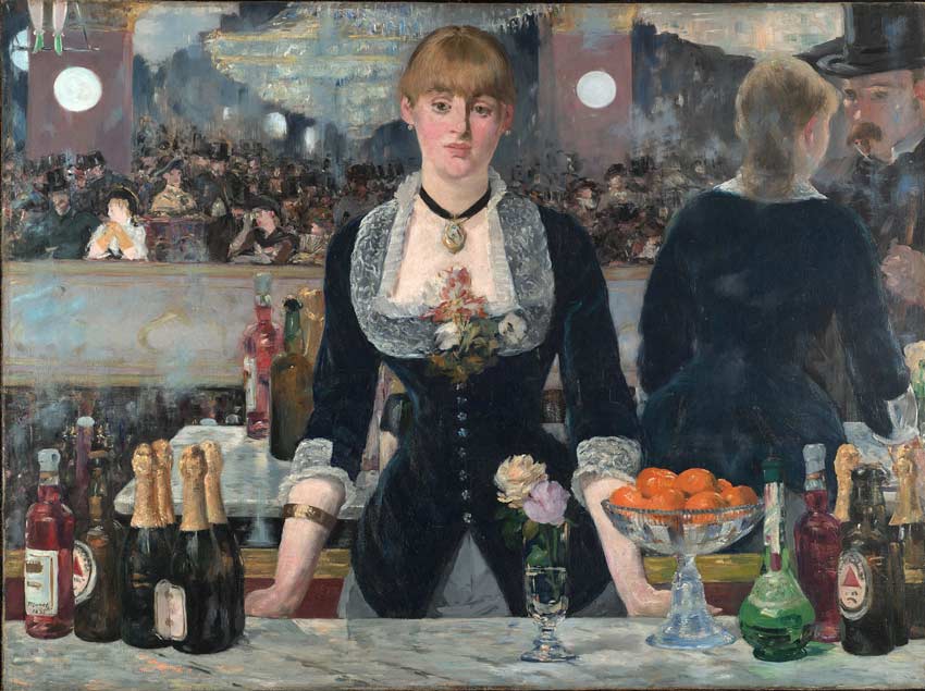Una mujer parada en la barra de un bar, observando. Hay botellas de licor y una vasija con frutas. al fondo se reflejan los asistentes en un espejo