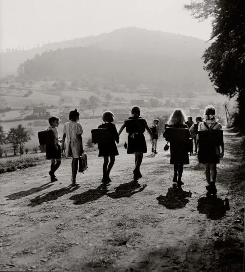 Fotografía: Robert Doisneau. Niños y niñas caminando dando la espalda hacia la escuela en una calle sin asfalto