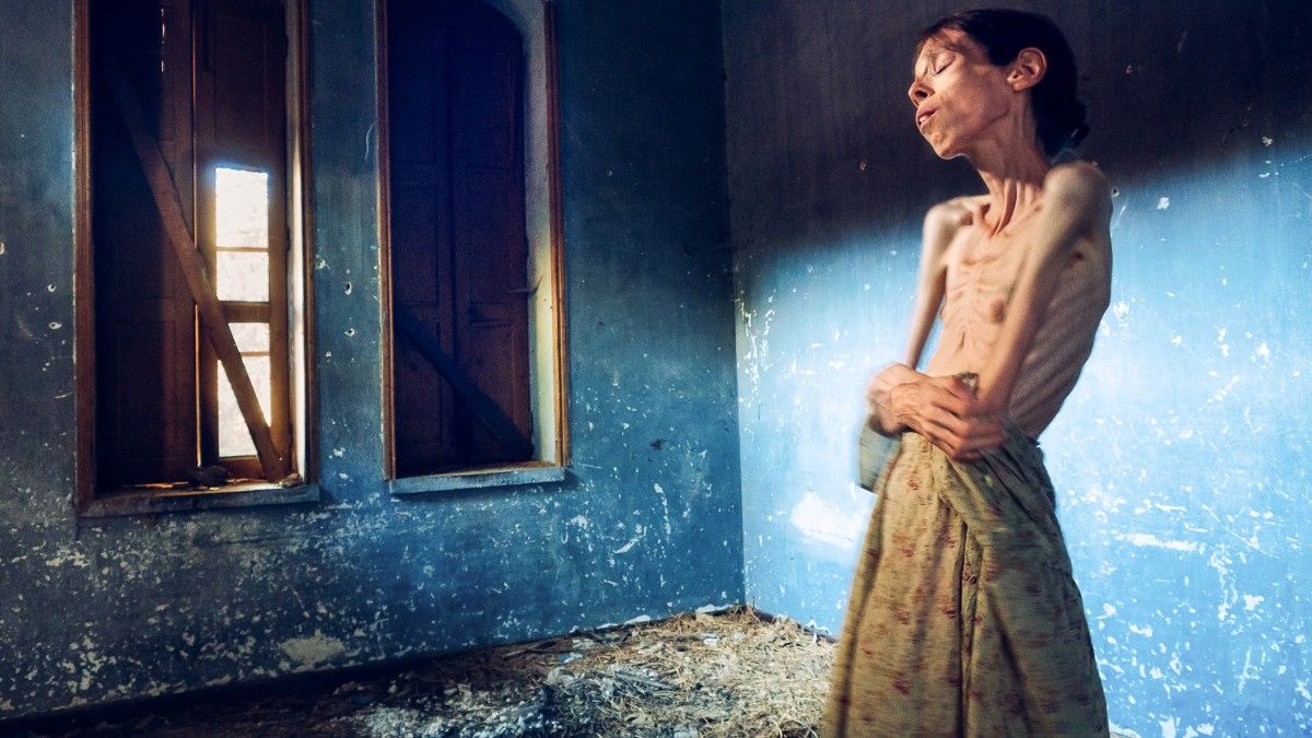 Autorretrato Lene Marie Fossen. En la foto una mujer que sufre anorexia de brazos cruzados en un cuarto con dos ventanas