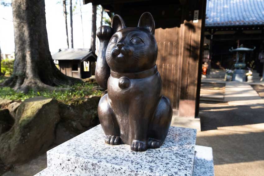 Estatua de color negro de un gato levantando su pata.