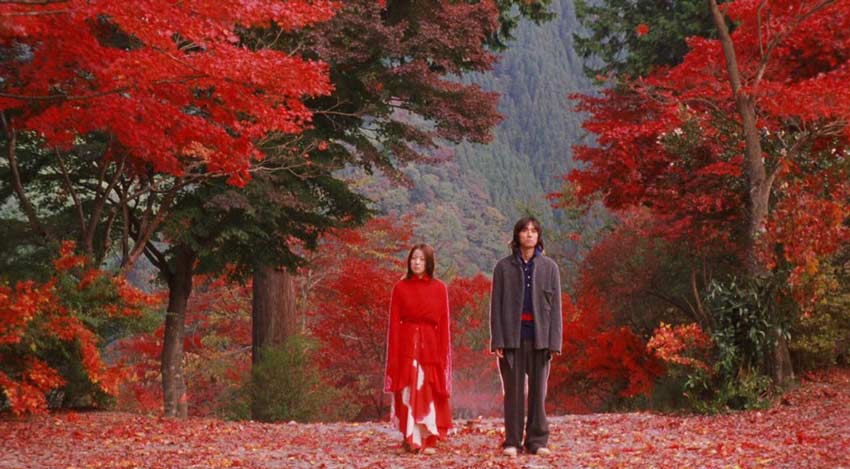 Leyenda japonesa del hilo rojo en el cine. Hombre y mujer parados en un bosque de árboles con hojas rojas.