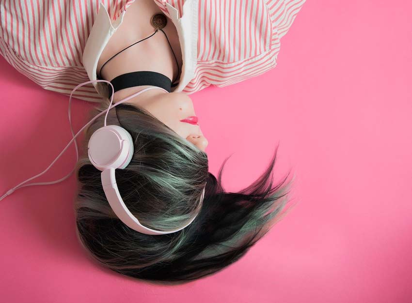 Fotografía de mujer escuchando música en un fondo rosa. Artículo: Psicología, significado de los colores