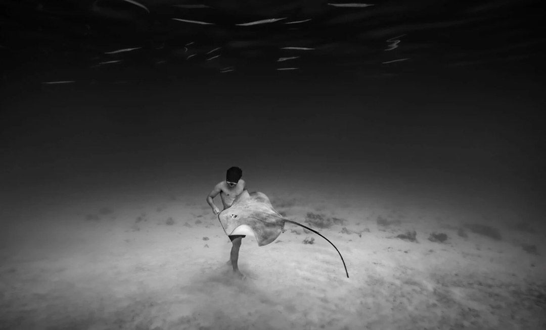 “Alone Together” de Cristina Mittermeier. Hombre bajo el océano con una raya marina en blanco y negro.