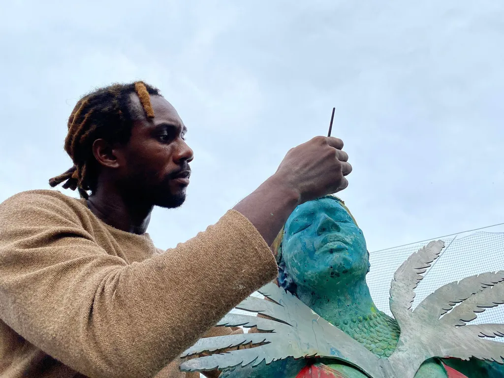 Fotografía del artista DiCaires Taylor terminando de pintar una escultura.